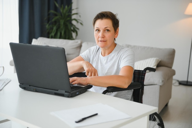 Positive elderly woman in wheelchair working on laptop IT freelancer online