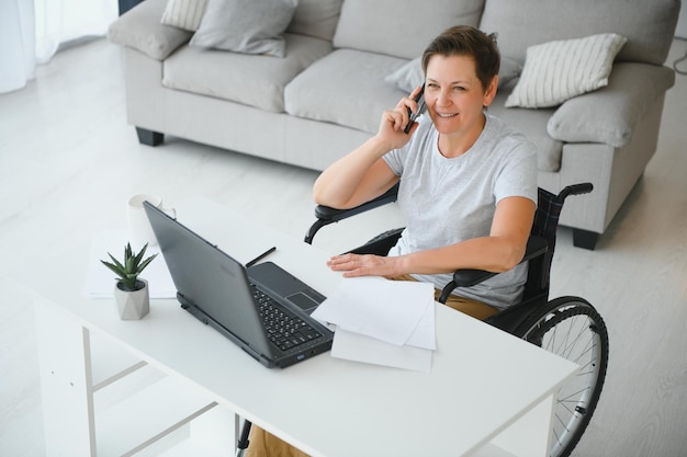 Positive elderly woman in wheelchair working on laptop IT freelancer online