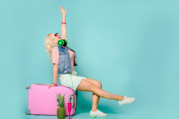 Позитивная эмоциональная женщина с розовым чемоданом на цветном фоне. Концепция путешествия.