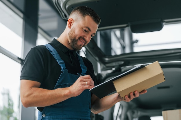 Positive emotions Delivery man in uniform is indoors with car and with order