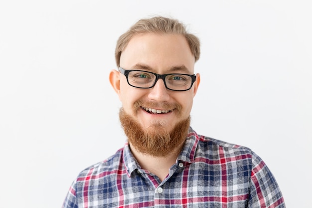 Positive emotions and people concept - young bearded man in glasses is smiling on white wall.