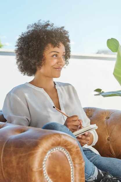 Positive ethnic woman writing thoughts in notepad