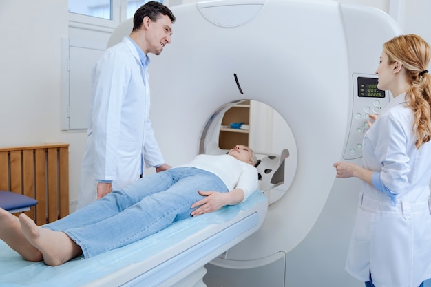 Positive experienced male doctor looking at his colleague and smiling while doing brain tomography