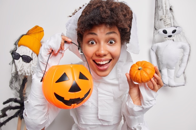 Positive female halloween character holds traditional pumpkins poses on October decorations carved jack o lantern prepares for party poses on white 