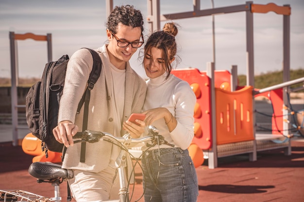 Photo positive female and her boyfriend smiling watching at mobile phone on a bike