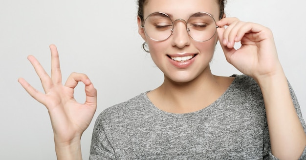 Positive female student wears grey sweater round glassesPeople