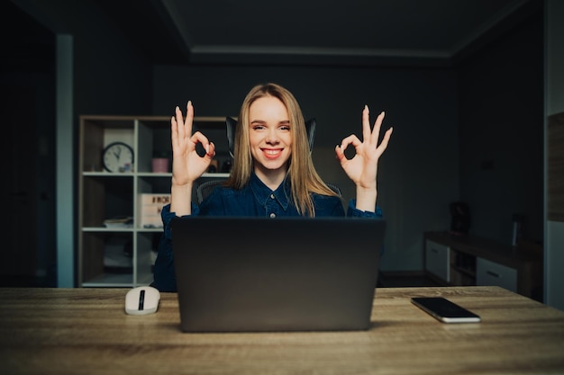 Positive freelancer woman sitting at home at a table with a\
laptop in a cozy room