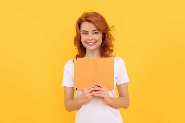 Positive girl hold copybook on yellow background reader