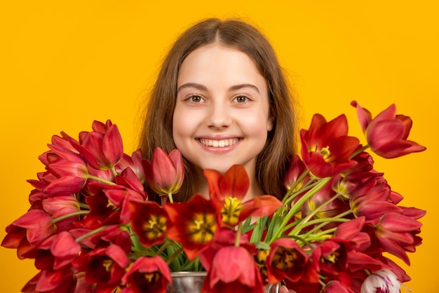 Позитивная девушка держит весенние цветы тюльпана на желтом фоне