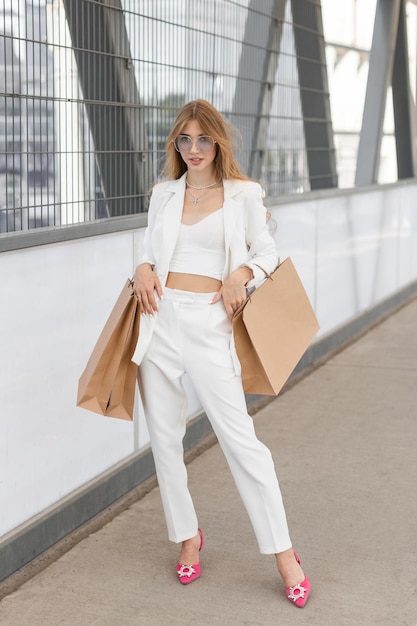 Positive girl is wearing in stylish suit walking at street after shopping with many paper bags