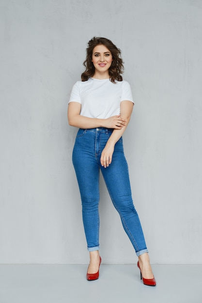 Positive girl in jeans, white t-shirt and red stilettos posing