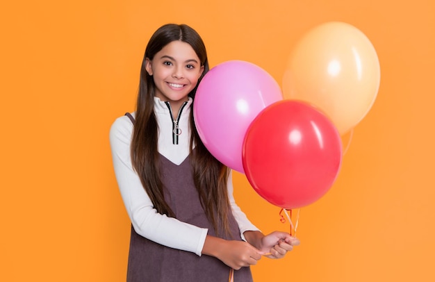 positive girl with party colorful balloons on yellow background
