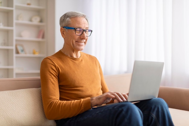 Positive grandfather sitting on couch with laptop