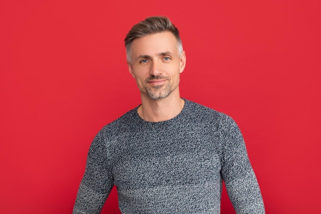 Positive grizzled guy in sweater on red background portrait