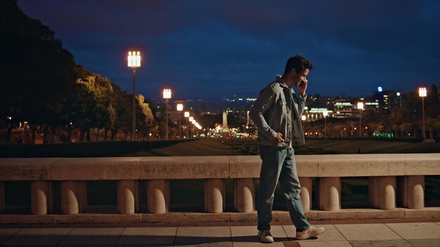 Positive guy speaking mobile phone at night city view smiling latin man talking