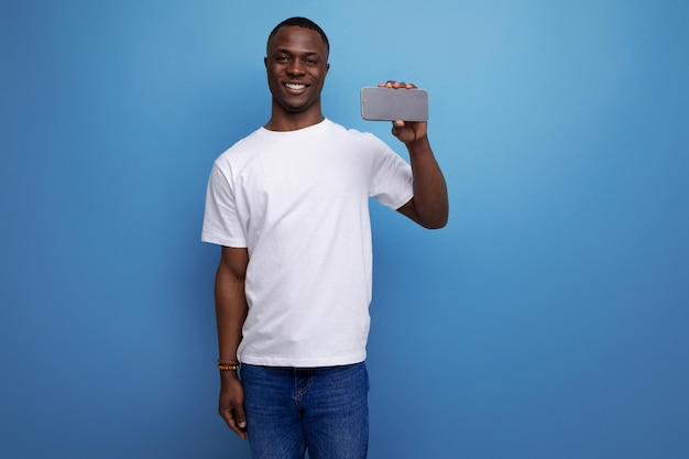 Positive handsome darkskinned young american guy in a white tshirt shows the phone