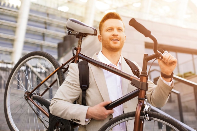 Positive handsome man looking upwards and carrying a bicycle on shoulder