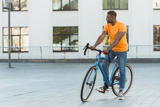 Positive handsome Nigerian man riding bicycle on street outdoors Active lifestyle concept