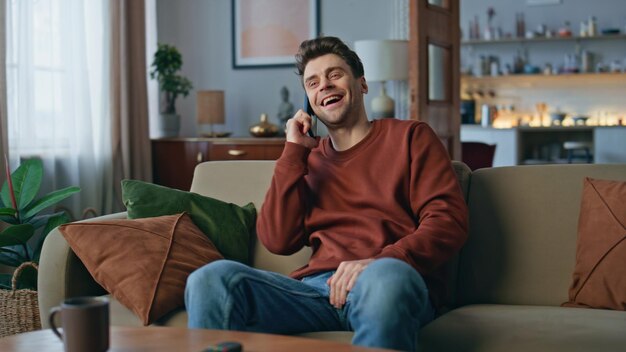 Positive hipster speaking mobile phone at home weekend happy man laughing couch