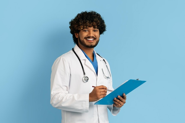 Foto dottore indiano positivo in uniforme che tiene in mano il blocco e sorride