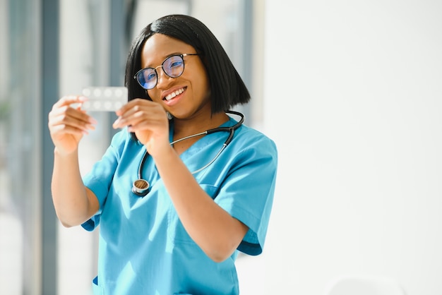 Positivo gioioso giovane donna afro-americana farmacista o medico, tenendo in mano le pillole