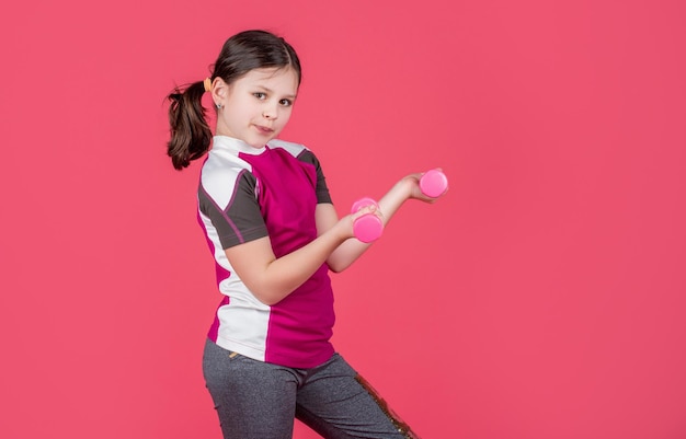 Positive kid hold fitness barbells on pink background copy space