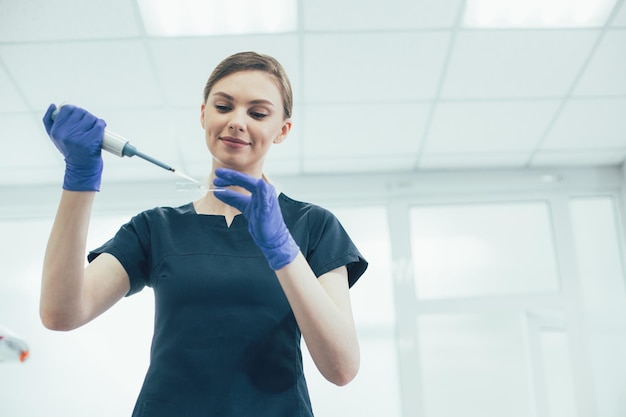 Positive lab scientist standing with a sample on microscope slide and holding an automatic pipette dispenser