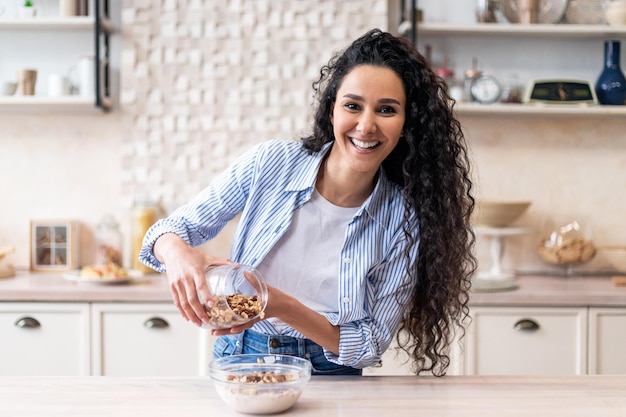 Positive latin woman pouring corn flakes in plate with milk having healthy breakfast on cozy kitchen