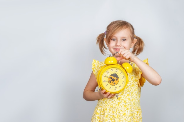 A positive Little Caucasian girl holds an alarm clock in her hand and smiles