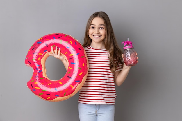 Positive little girl enjoying her vacation holding rubber ring and holding fresh cocktail