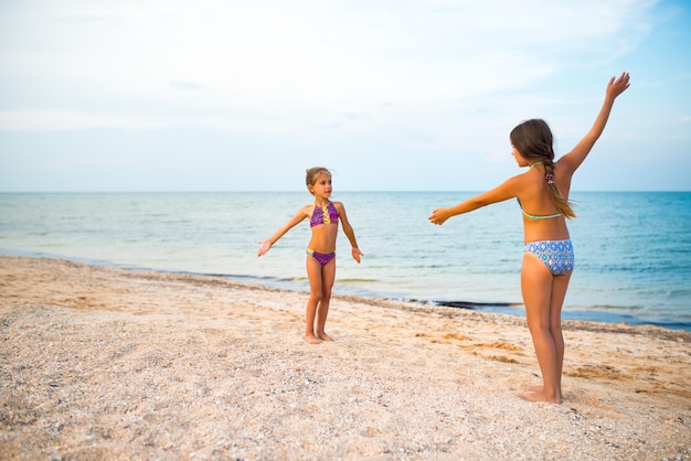 ポジティブな小さな女の子の姉妹は、晴れた暖かい夏の日の夏休み中に砂浜でアクティブなゲームをプレイします