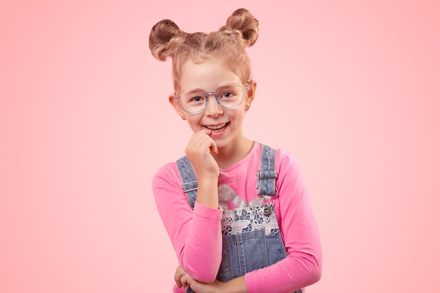 Positive little schoolgirl in casual denim overall and eyeglasses looking with interest