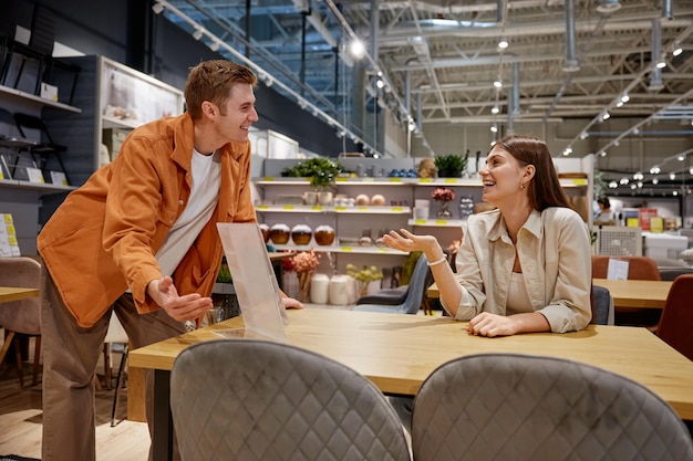 Positive loving couple testing new furniture for dining room at store