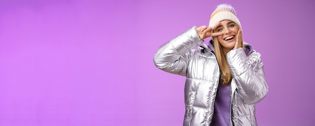 Positive lucky cute blond girl having fun winter vacation in silver glittering jacket hat posing