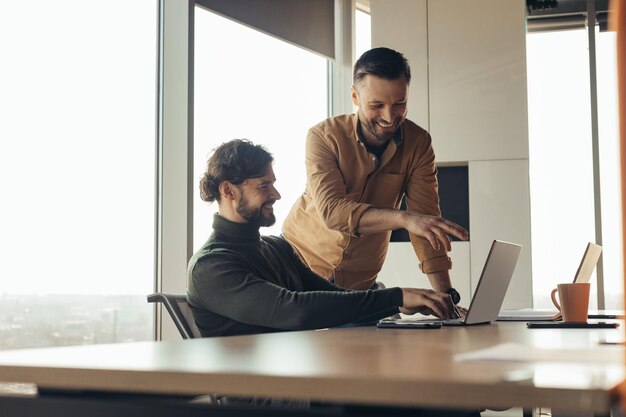 Positive male employees discussing business project using laptop computer brainstorming for ideas at