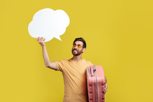 Positive male tourist with travel suitcases holding empty speech bubble above his head copy space yellow background