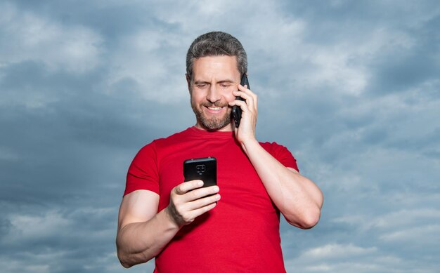 Позитивный мужчина разговаривает по телефону на фоне неба