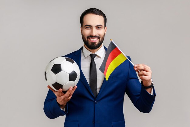 Positive man holding flag of germany and soccer black and white classic ball and watching match