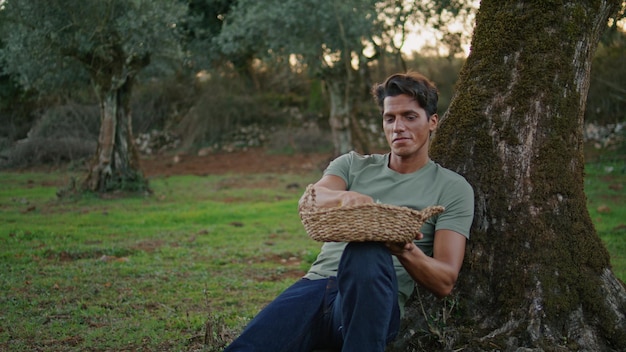 オリーブの木の風景を嗅ぐポジティブな男性が休憩を持つ幸せな農家をクローズアップ