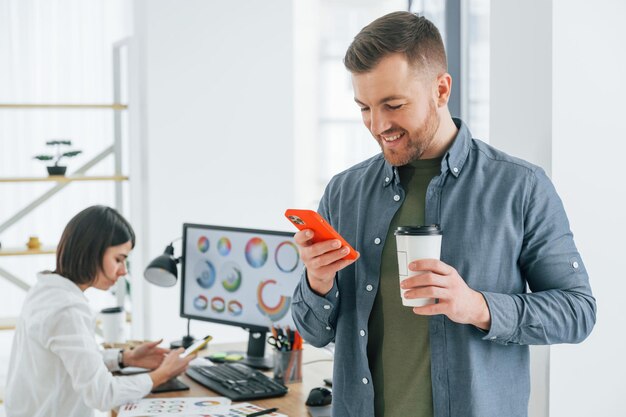 Positive man standing in front of woman that sitting by the\
table two designers working together in the office