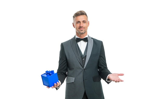 Positive man in tuxedo and bow tie hold present box isolated on white background