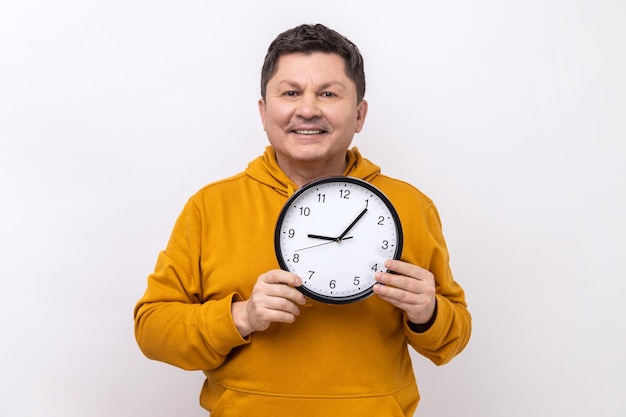 Positive man wearing blue casual shirt showing holding big wall clock looking at camera with smile