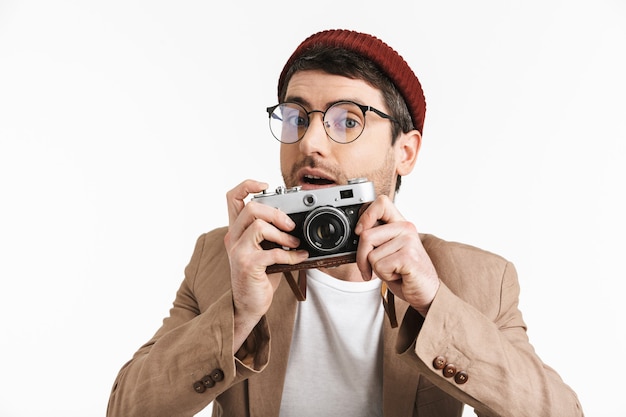 positive man wearing hipster hat rejoicing while holding and photographing on retro front isolated over white wall