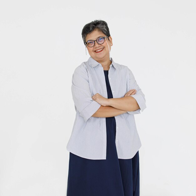 Positive mature Asian female in glasses crossing arms and looking at camera with smile against gray background