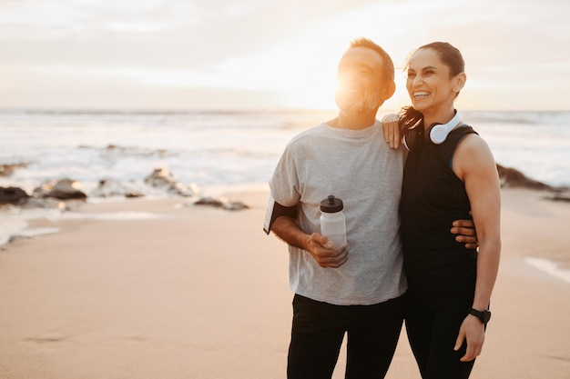 Positive mature european couple hugs in sportswear rest from workout with bottle of water together