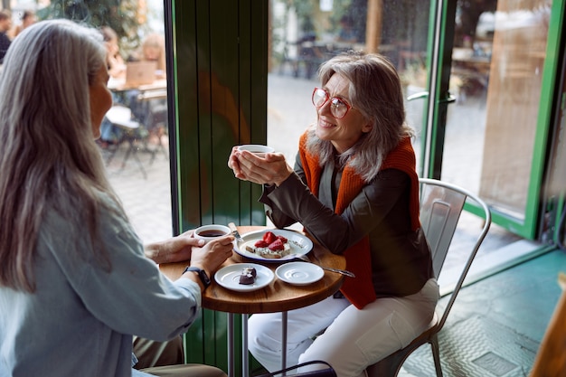 La donna matura positiva e la compagna con i capelli grigi si godono un drink a tavola in un accogliente caffè