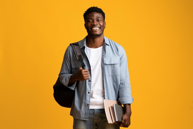 Photo positive millennial black man student with books on yellow