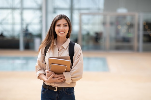 Positive millennial mixed race woman brunette student in casual with backpack hold books go to