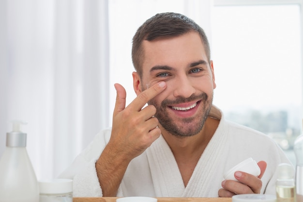 Positive mood. Delighted cheerful man smiling while applying facial cream