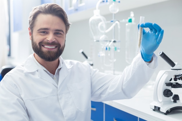 Positive mood. Happy nice successful biologist holding a test tube and smiling while looking at you